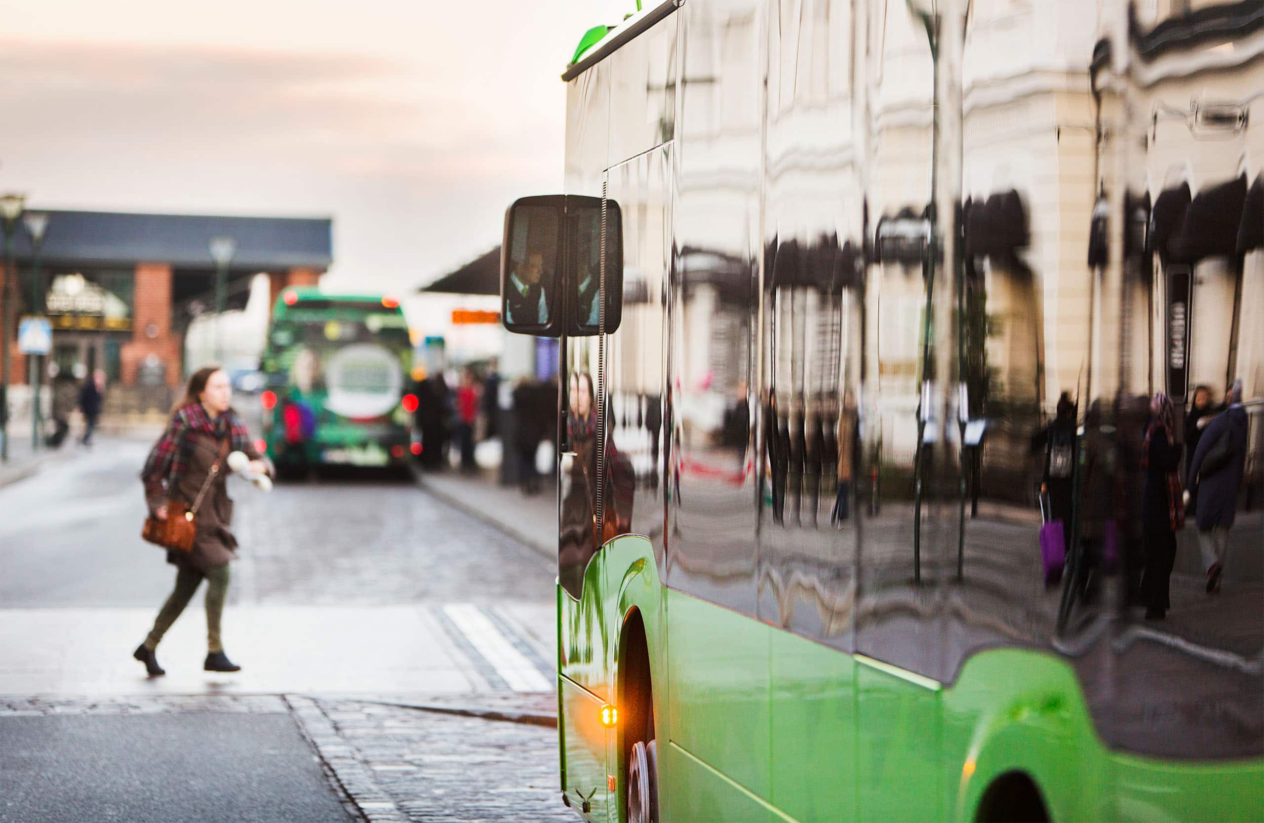 Kvinne krysser gaten foran en grønn buss